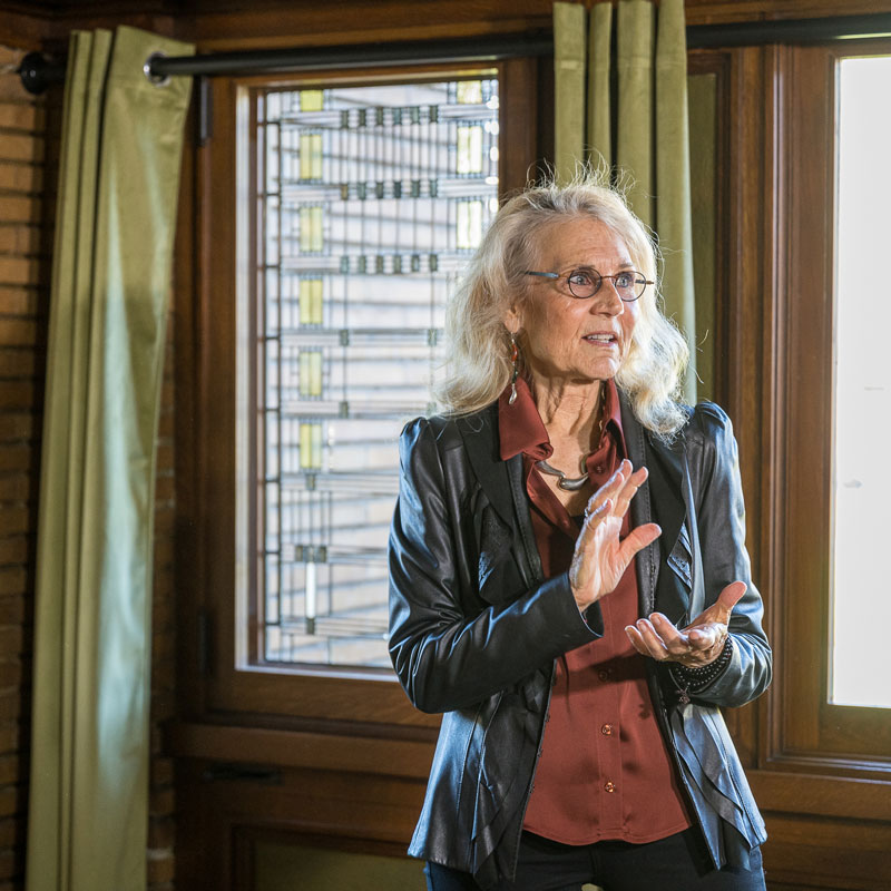 Docent uses her hands as she talks against a backdrop of Martin House Art Glass Windows